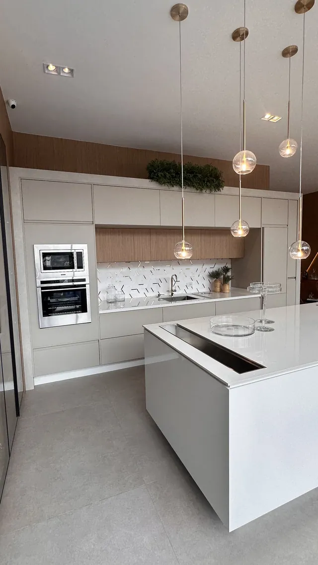 Cozinha planejada com ilha branca, cooktop, eletrodomésticos embutidos e pendentes acesos