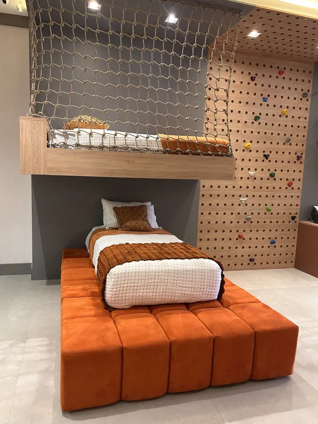 Quarto infantil com cama baixa, mezanino protegido por rede e painel perfurado para escalada
