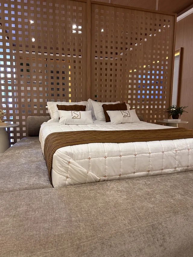 Quarto de casal com painel ripado vazado em madeira e iluminação quente