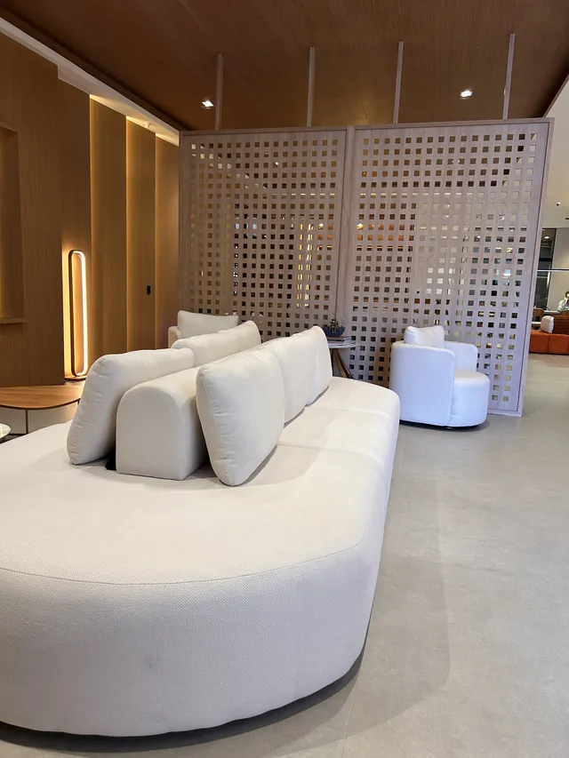 Sala com sofá curvo branco, poltrona e divisória vazada, painéis de madeira